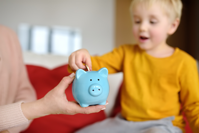child dropping money in to a blue ceramic money box